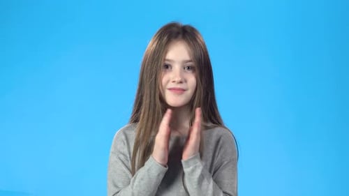 Blonde Teenage klatscht in die Hände, lächelt, schaut in die Kamera.