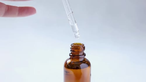 Dropper Dispensing Liquid into Amber Glass Bottle