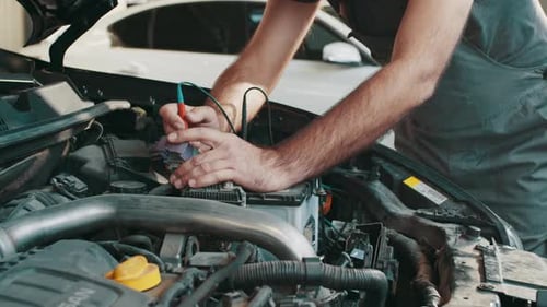 Mechanic Checks Engine with Voltmeter Inside Car Shop