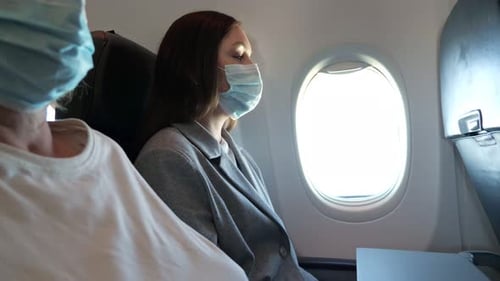 Young Woman Wearing Mask on Airplane, Looking Out Window