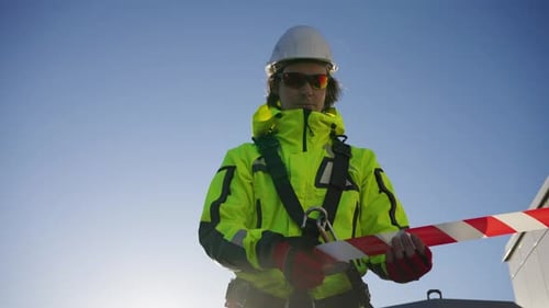 Alpinista industrial em um capacete branco encerra uma área de trabalho com fita de sinalização