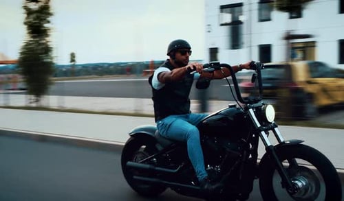 Man Rides Motorcycle on Road in Urban Area