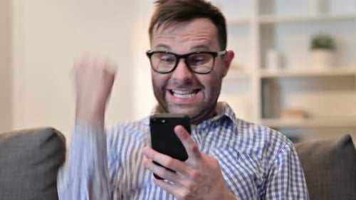 Enthusiastic Man Cheers While Using Smartphone on Couch