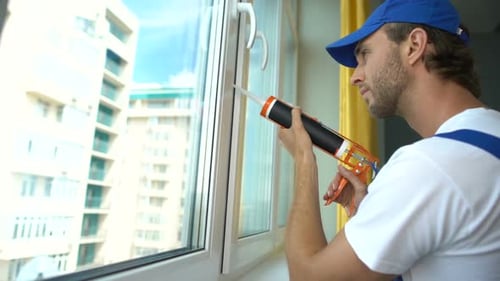 Homem usa adesivo de silicone com pistola de cola para reparar janelas desgastadas, isolamento acústico