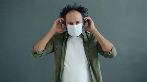Man Putting On Surgical Mask and Holding Up Peace Sign