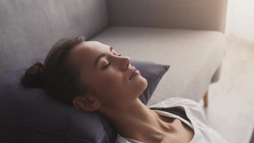 Young Peaceful Woman Meditating at Home Leaning on Sofa Head Lying on Pillow Close Up Free Space