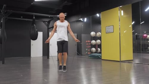 Männlicher Boxer mit Springseil. Kämpfer macht Springseilübungen im dunklen Fitnessstudio