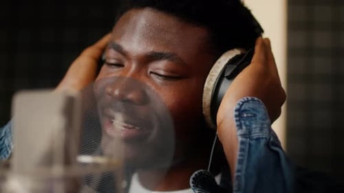 African American Male Singer Wearing Headphones Singing To Microphone In Music Studio
