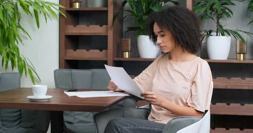 Concentrated Woman African American Student Freelancer with Paper Work Sitting at Table in Office