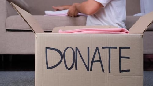 Junge Frau steckt zu Hause Kleidung in eine Spendenbox, um den Armen zu helfen. Spenden-Konzept.