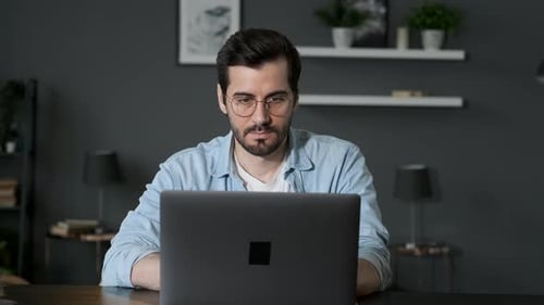 A young Greek Man with a Beard and Glasses Works at Home, Typing on a Computer Keyboard