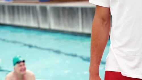 Lifeguard Standing Poolside With Swimmers in Background