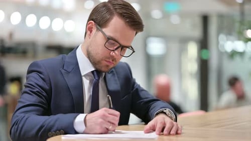 Focused Businessman Writing at Desk in Modern Office