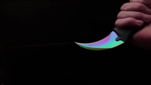 Hand Holding a Colorful Knife in Dark Setting