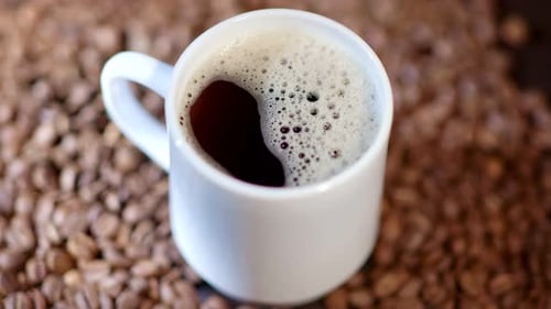 A Cup Filled with Tasty Fragrant Coffee is Standing Amidst Many Coffee Beans