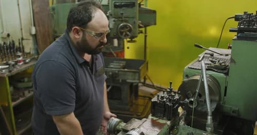 Caucasian male factory worker at a factory sitting at a workbench and operating machinery