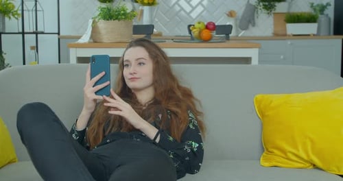 Woman Relaxing on Sofa Using Smartphone at Home
