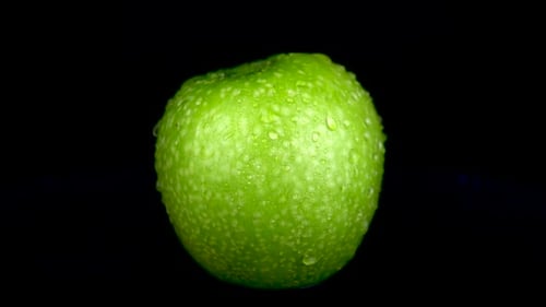 Water Is Sprayed on a Green Apple. On a Black Isolated Background