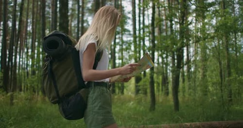 A Young Woman with a Map Is Walking Through the Forest Traveling with a Backpack in Slow Motion