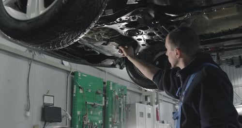 Mecánico de automóviles trabajando debajo del automóvil en el garaje del concesionario.