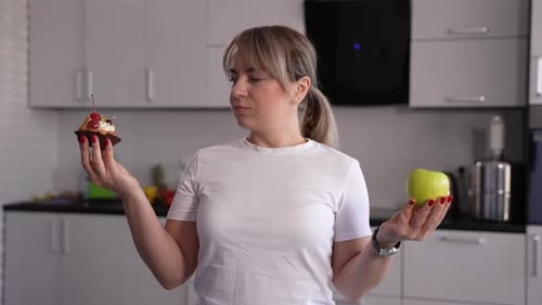 Woman Chooses Between Apple and Cupcake in Kitchen