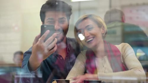 Video call. Happy couple using phone in cafe indoors