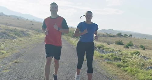 Tracking Slow Motion Shot of Sportive Couple Jogging Outdoors in the Morning Trail Running