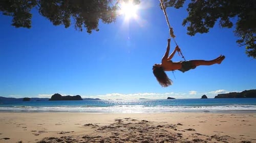 Woman swinging on rope swing by the ocean