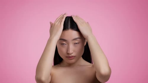 Young Woman Styling Hair on Pink Backdrop