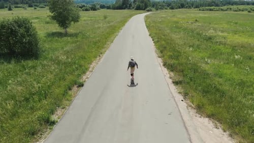 Man Rides at Straight Road on Longboard at Sunset Time Aerial . The Guy Rides a Longboard on the Way