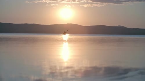 Kayaker Paddling Across Calm Lake at Sunrise