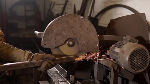 Nahaufnahme der Hände eines Mannes, der eine Metallstange in der Nähe einer Säge hält