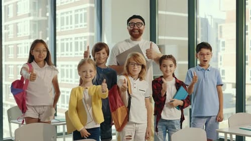 Portrait of the Children Stand with the Male Smiled Teacher in the Middle of the Class and Show a