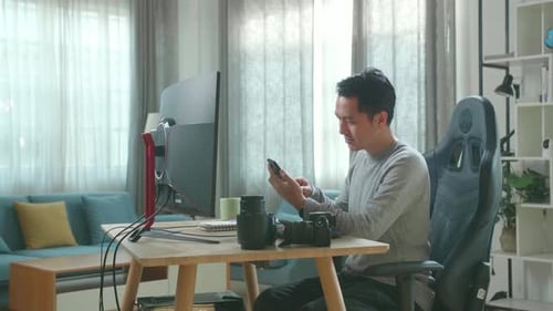 Man Using Smartphone at Desk with Computer