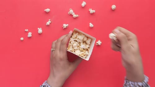 Top View of Women Hand Eating Popcorn on Red Background