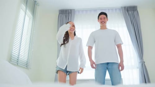 Happy Young Couple Dancing on Bed Together