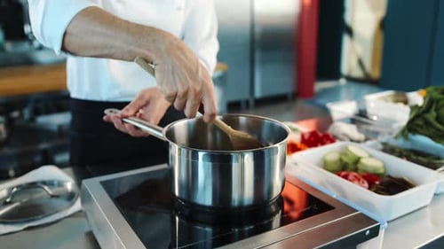 Close-up: The chef stirs the ingredients into a saucepan. The process of preparing food