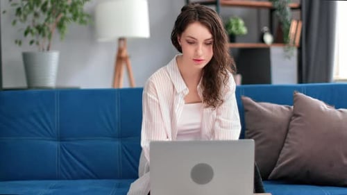 Young Woman Using Laptop on Blue Couch at Home