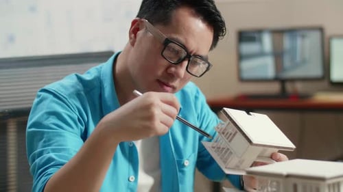 Close Up Of Asian Man Engineer Thinking While Holding Paper Model Of House At The Office