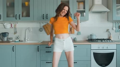 A Beautiful Woman in White Shorts is Relaxing at Home Dancing in the Kitchen