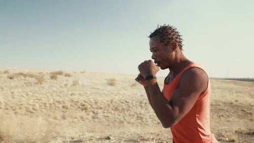 Black Man of Athletic Build is Engaged in Training Outdoors Jogging and Boxing Side View