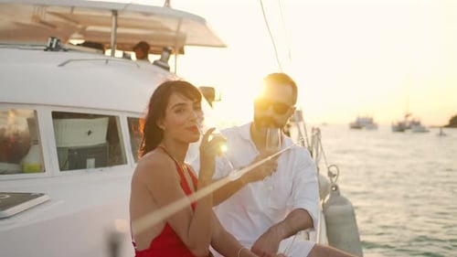 4K Caucasian couple drinking champagne while catamaran boat sailing in the sea at summer sunset.