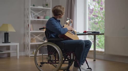 Side View Portrait Talented Disabled Caucasian Man Playing Guitar Sitting in Wheelchair at Home