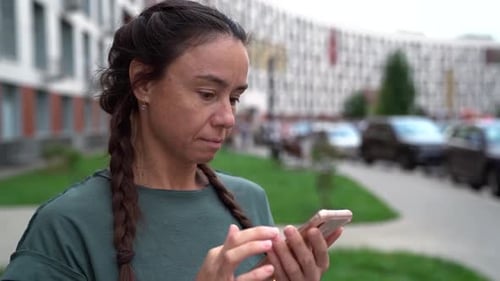 Woman Is Reading Message in Mobile Phone and Surprising, Googling Eyes, Standing Outdoors in City