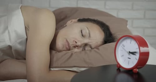 Woman Sleeping Peacefully Next to Red Alarm Clock