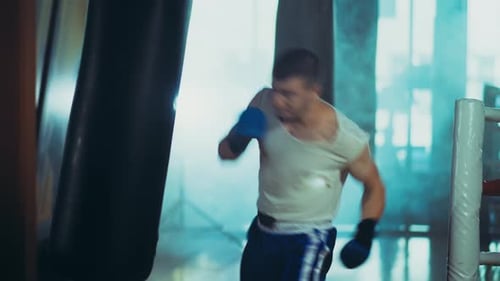 Athletic Young Man Punches Heavy Bag in Gym