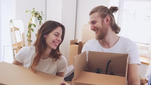 Schönes glückliches kaukasisches Paar, das in Zeitlupe Kisten mit Sachen in ihrer neuen Wohnung hält