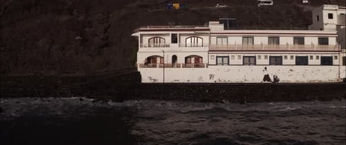 Tiro de Drone de um jovem sentado na varanda de uma vila costeira