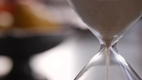 Hourglass sand falling in slow motion neck close up