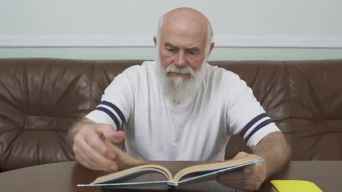 Senior Man Reading Book at Wooden Table